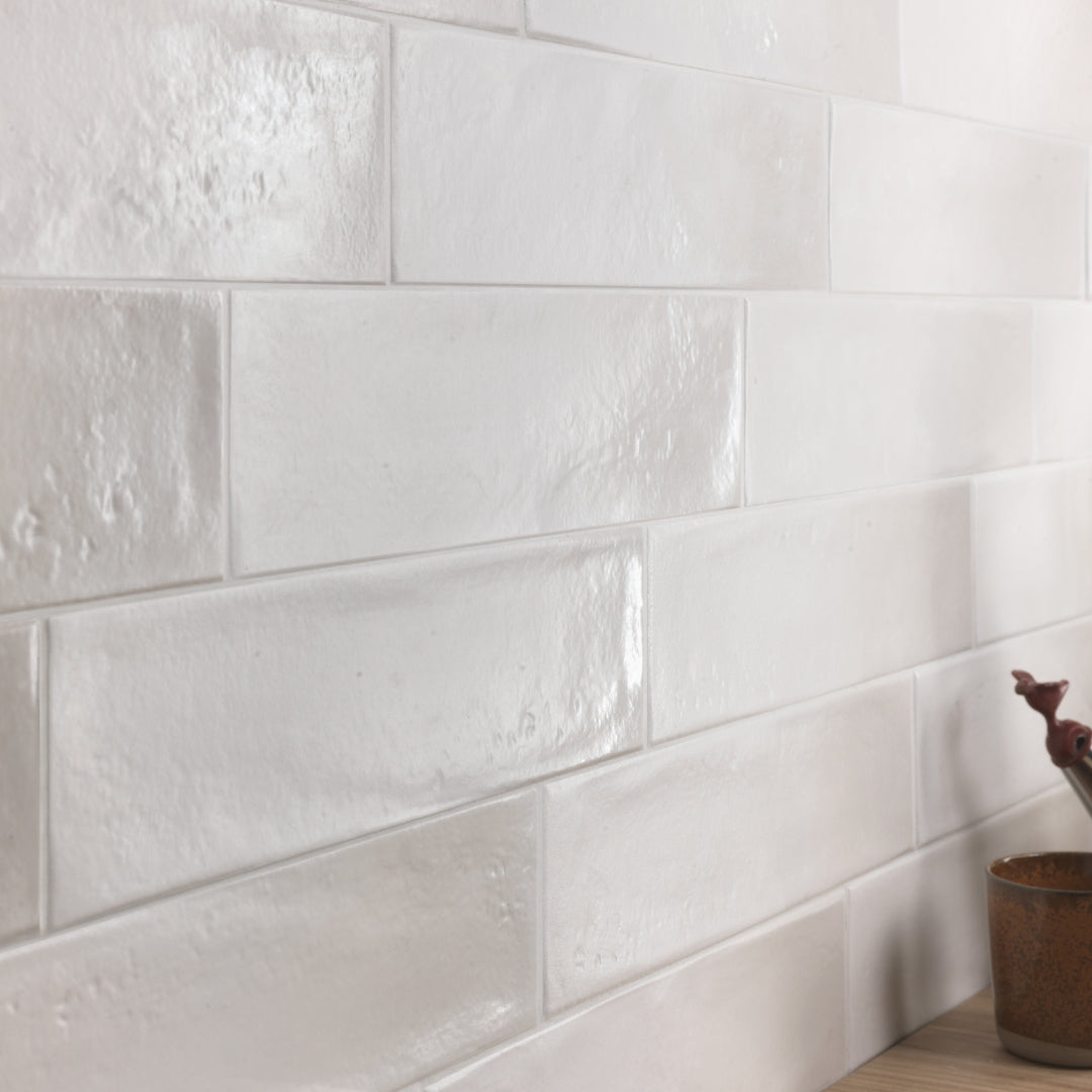 A close up of a tile install where the tiles are light grey 3x12 glossy variated colour tile. 