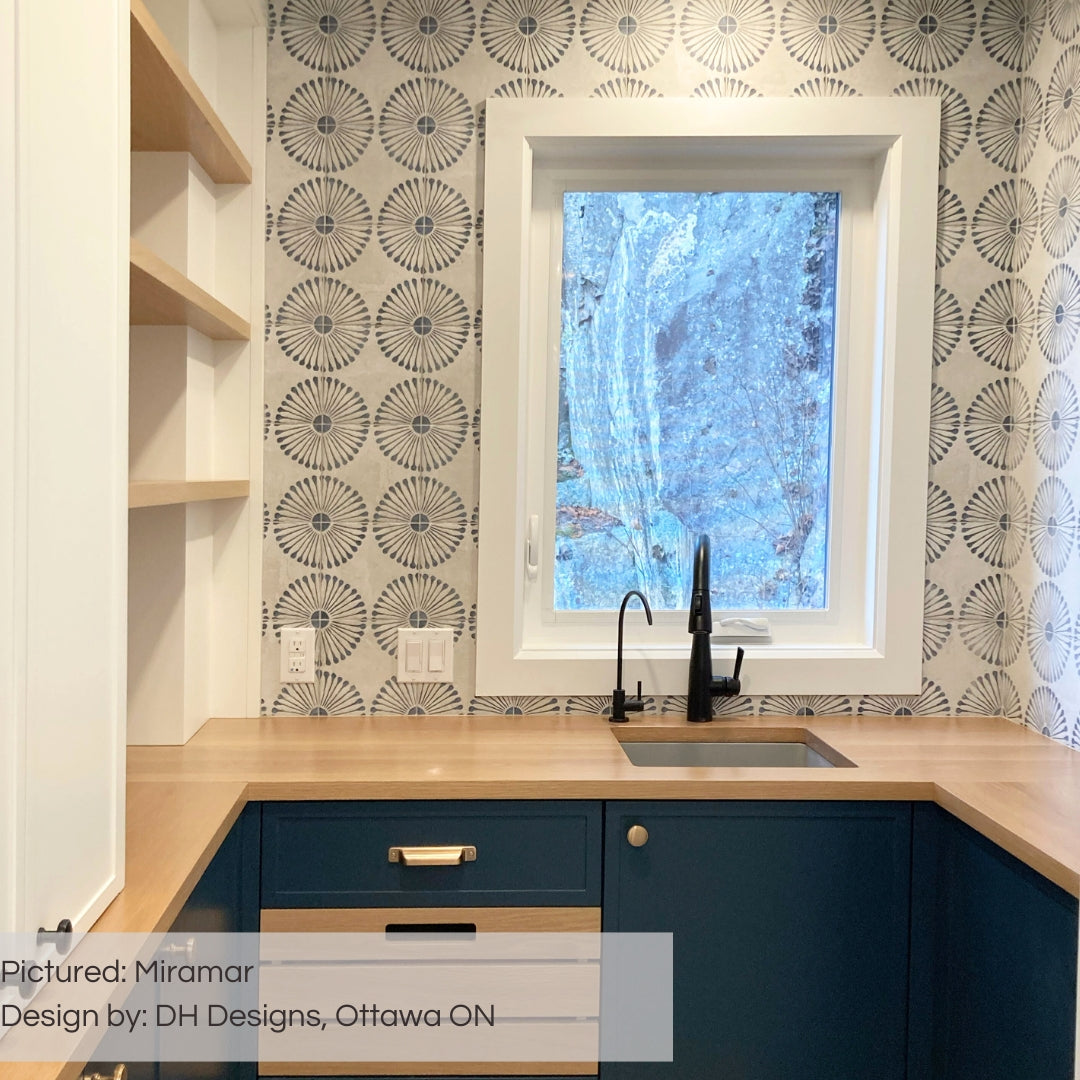 A stunning pantry with navy lower cabinets, and light wood counters and open shelving. the walls are tiled with miramar 8x8 flower burst circle pattern blue and grey tiles. 