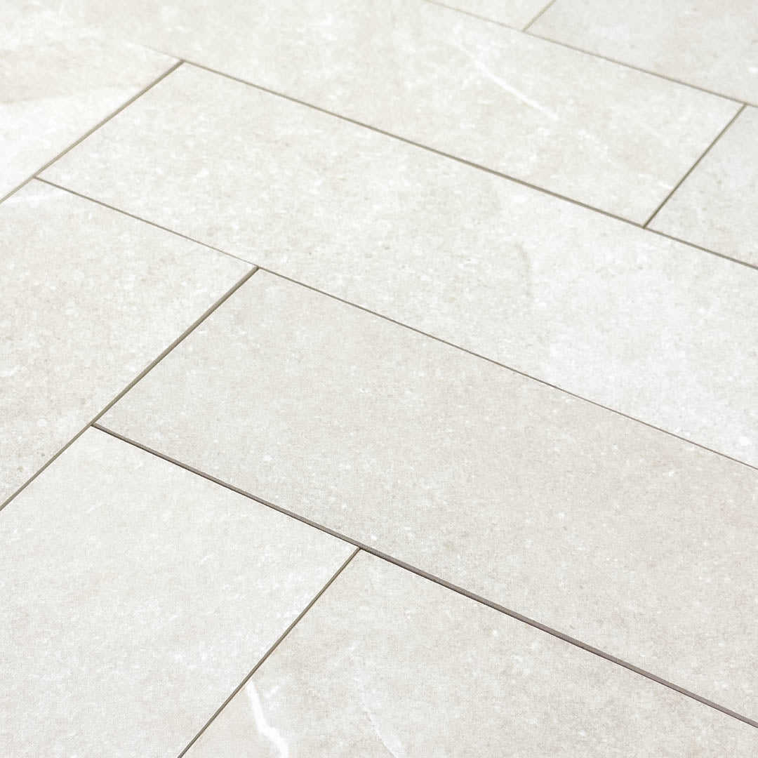 Angled close up of a group of stone look 4x12 matte tiles in light grey laid out in a herringbone pattern to show the pattern and finish.