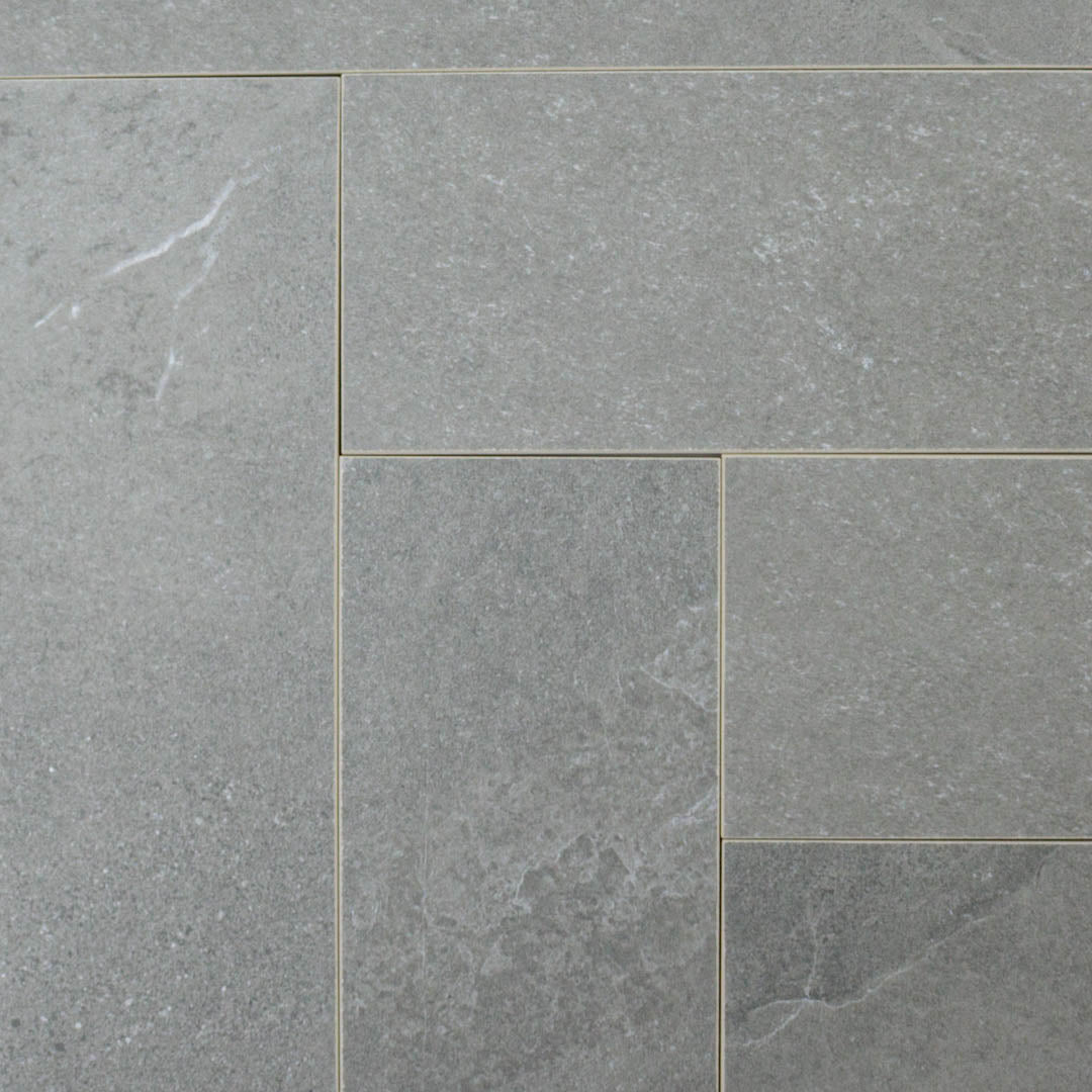 Ariel shot of a group of stone look 4x12 matte tiles in dark grey laid out in a herringbone pattern to show the pattern and variance where the corners meet.