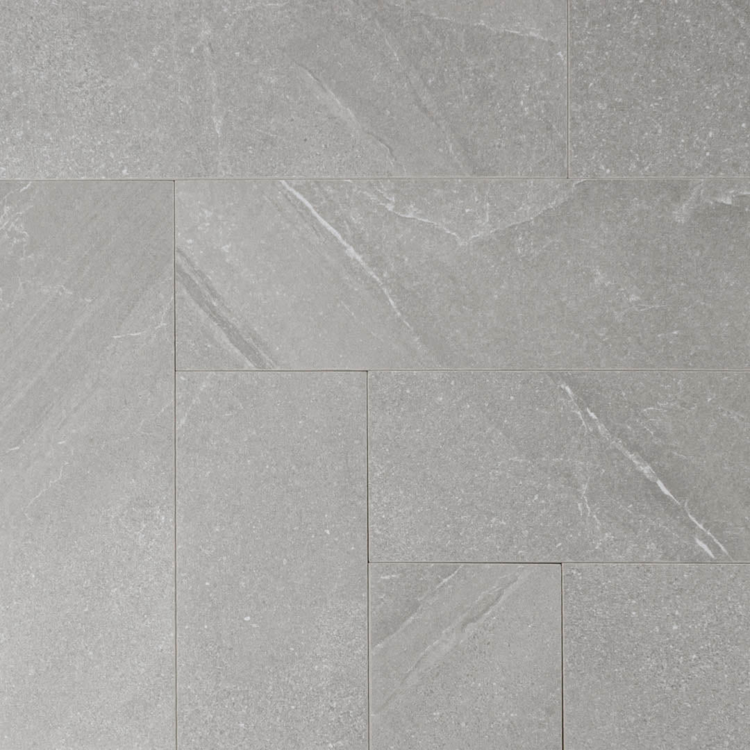 Ariel shot of a group of stone look 4x12 matte tiles in taupe laid out in a herringbone pattern to show the pattern and variance where the corners meet.