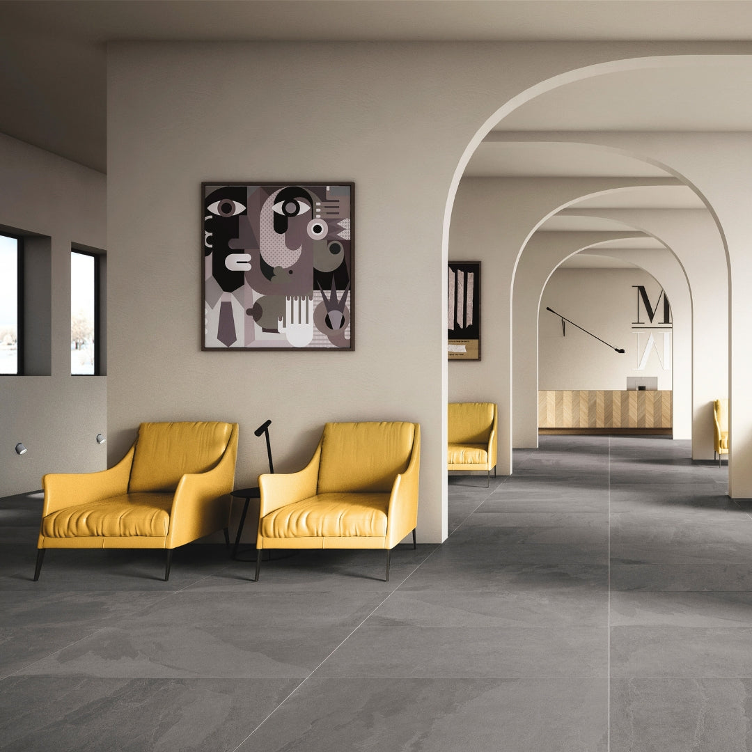 A modern commercial waiting area with grey arched walls, modern art and yellow chairs. the floor tile is a slate look grey large tile. 