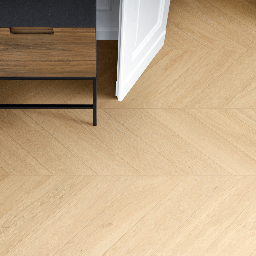 A close up of a tiled floor using a light sandy wood toned tile in a chevron shape to give the floor a geometric pattern.